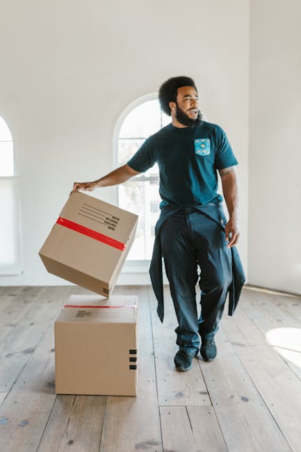 A person wearing a grey hoodie is assembling furniture using a screwdriver, working on a wooden tabletop during a home removal process. The individual is tightening screws into pre-drilled holes, with