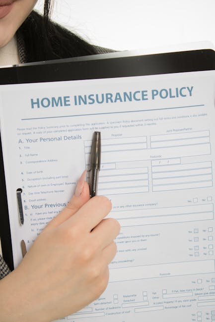 A person’s hand holding a silver pen is positioned above a printed home insurance policy form, with various sections including personal details, previous insurance, and property information visible.